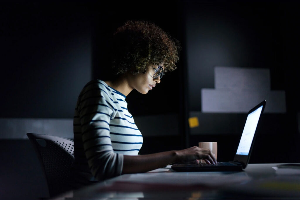 Image of a focused female student studying in the dark, independently building websites for her portfolio and gaining real-world experience in web development.